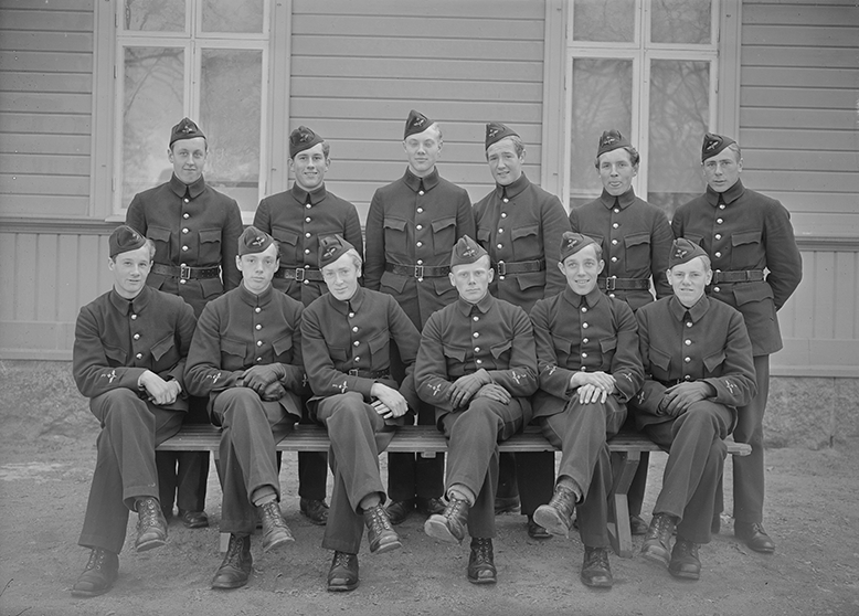 Volontärer på F 3 Östgöta flygflottilj, 1941. Del av grupp, tolv stycken unga män. Grupporträtt framför byggnad.