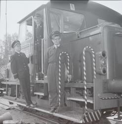 Tre jernbaneansatte står på lokomotiven til den første vogne