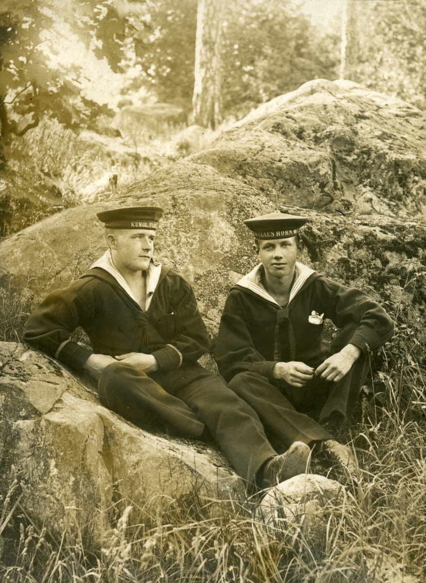 Två sjömän sittandes ute i naturen. På mössbanden finns texten KUNGL. FLOTTAN samt CLAES HORN.
