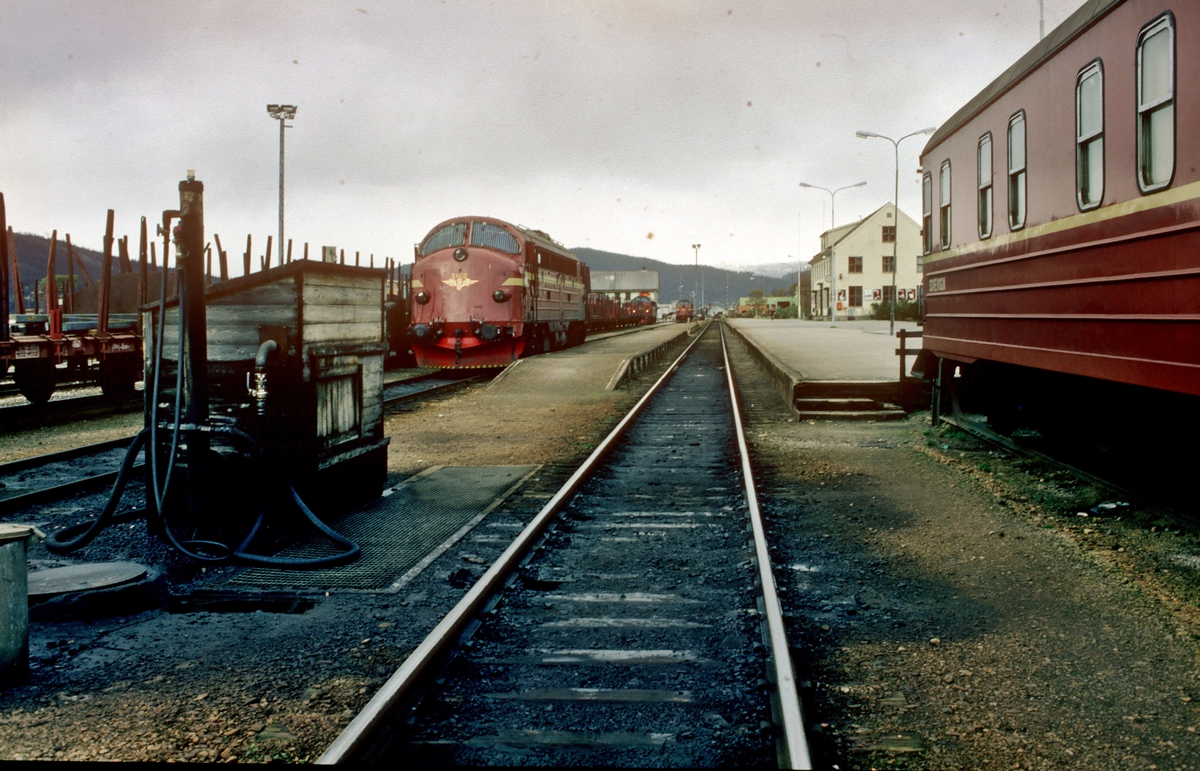 Mo i Rana stasjon våren 1983. Til høyre står sovevogna som har blitt skiftet ut av nattoget. Til venstre ser vi fyllingsanlegget for diesel. Noen lokomotiver av type Di 3 står rundt på stasjonsområdet.