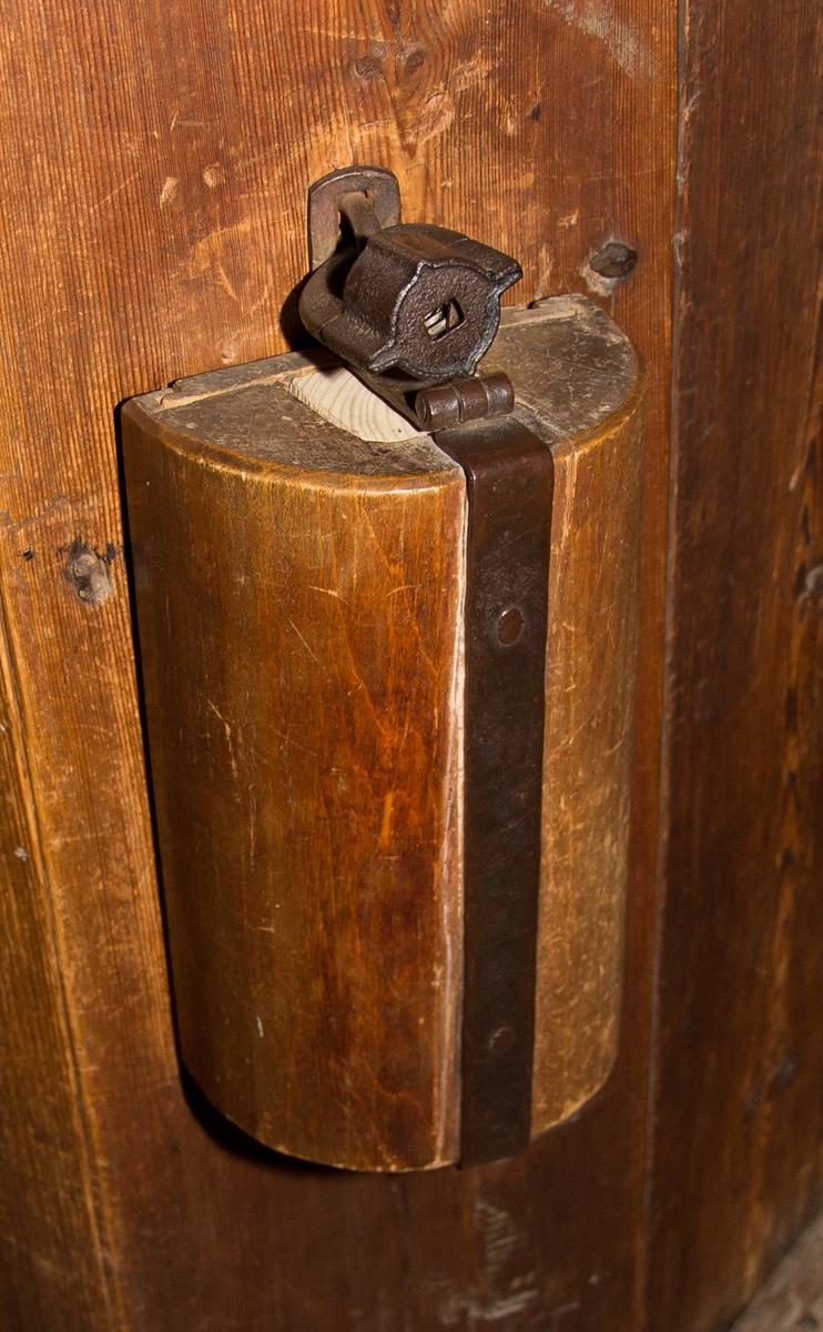 Fattigbössa av trä, brunmålad, halvcylindrisk med vertikalt järnband för låsning. Äldre hänglås.