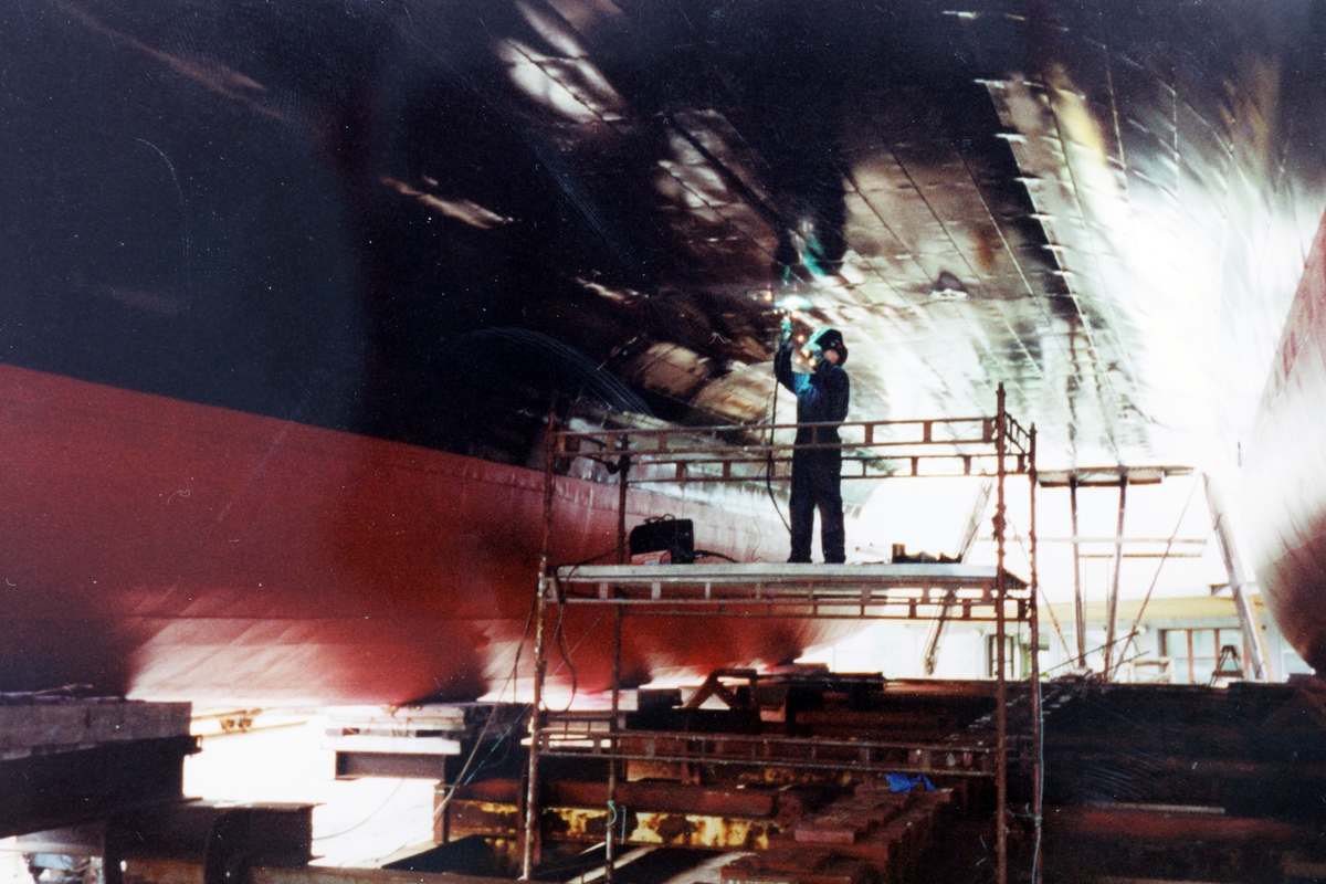 Sveiser arbeider på et stillase under bunnen av en hurtigbåt.