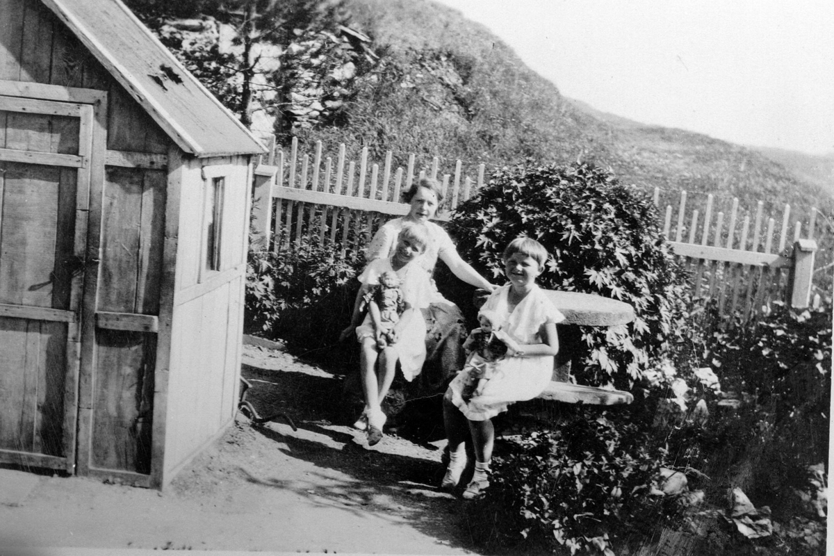 Valborg Schneider med døtre, fotografert i hagen. Stabburshaugen i Harstadgårdsbakken i bakgrunnen.