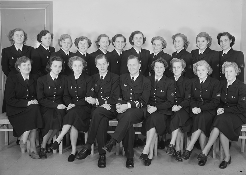 Elever vid signallottakursen på F 3 Östgöta flygflottilj, 1951. Del av klass, 18 kvinnliga elever tillsammans med två militärer. Grupporträtt inomhus.