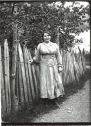 En ung dame poserende ved et gjerde, under et tre.
