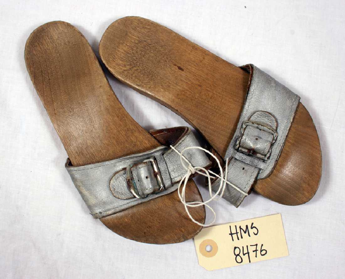 Et par "slip-in" sandaler med bred sølvfarget lærreim over vrist, metallspenne, nagler i såle,  heltresåler med gummibelegg under. 