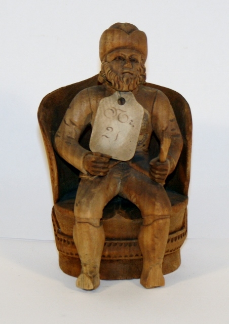 Figur av mann med skje i hånden, sittende i stol.