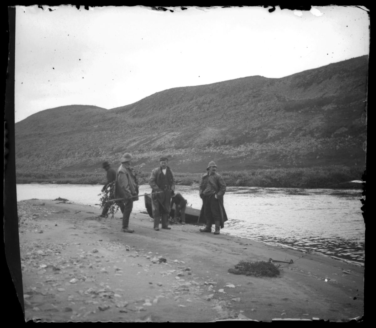 Fem arbeidskarer i fjæra, ved elvemunningen til Vesterelva i Syltefjord. De har antakelig nettopp kommet i land fra fisketur, de har fremdeles sydvester på