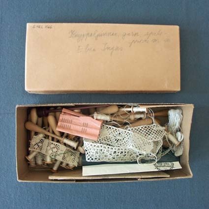 En ask med knyppeltillbehör som tillhört Elna Ingers. På locket står "Knyppelpinnar, garn, spetsprover mm Elna Ingers". I asken ligger också två kuvert och ett brev, daterade 1949 och 1955. Med brevet (1955) skickades ett utlovat knyppelmönster.