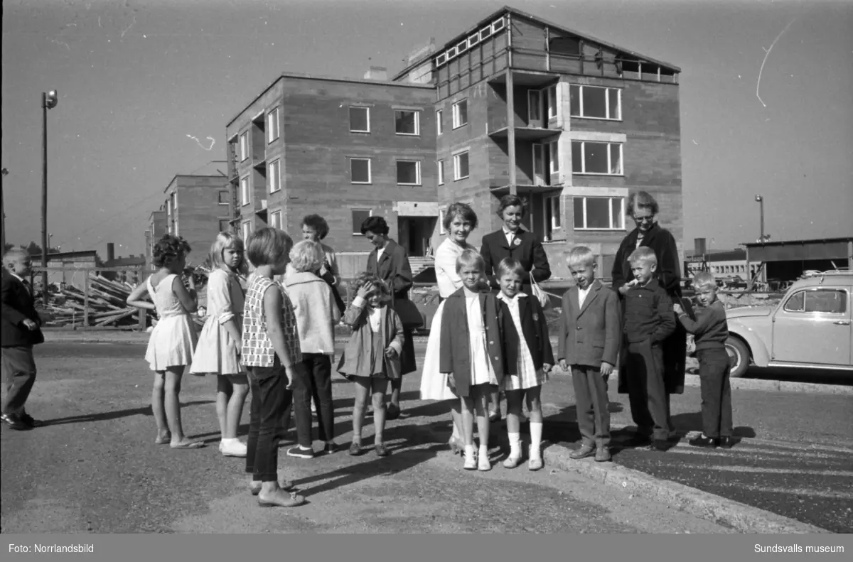 Skolstart på Sankt Olofsskolan. Förväntansfulla barn och mammor samlas utanför skolan. I bakgrunden syns kvarteret Tegen där bygget av det så kallade Långholmen pågår.