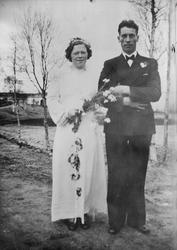 1 brudepar. Bruden er kledd i lys lang kjole. I hendene hold