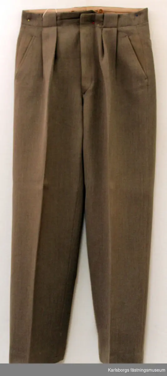 Långbyxa m/1939 - major, Signal. tillverkas av gråbrungrön diagonaltyg. Byxorna är försedda med midjeband med knappar och knapphål. Blixtlås i gilfen. Samtliga byxor är försedda med sid- och bakfickor.