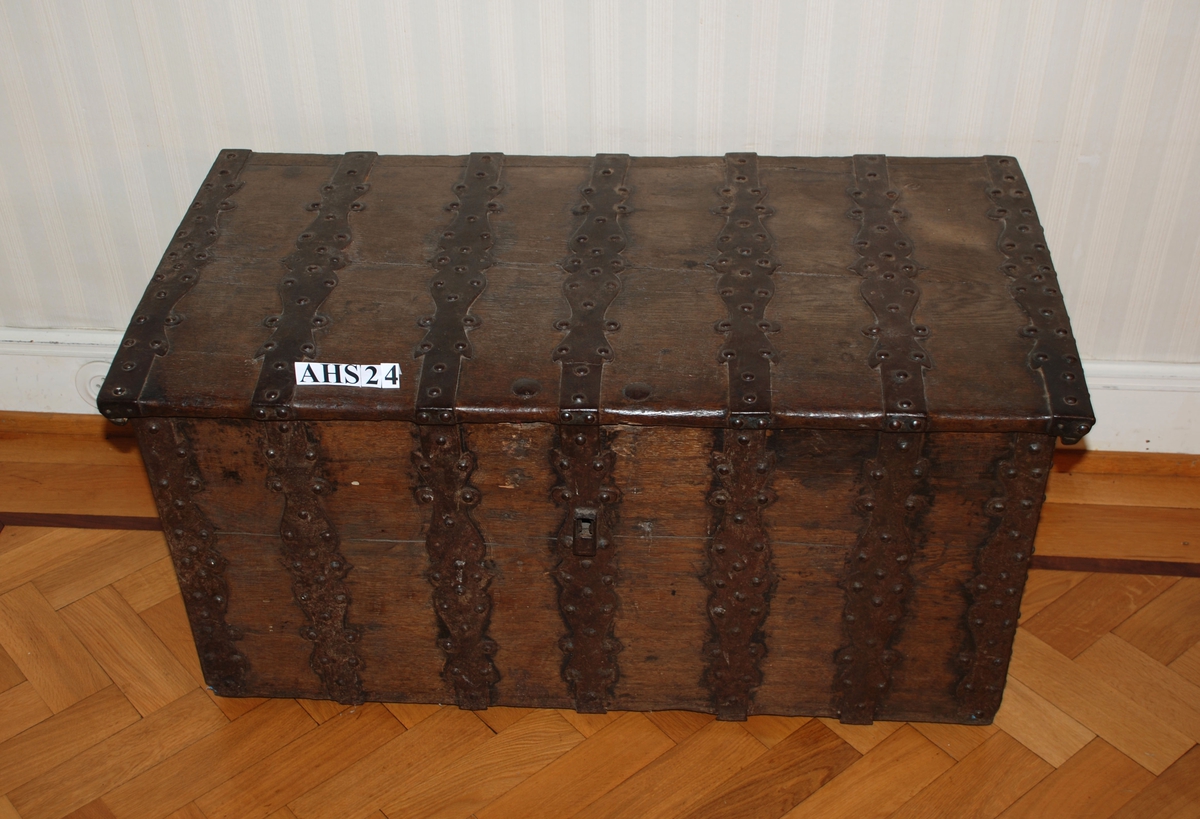 Kiste med rike jernbeslag. Flatt lokk, sidene svakt utadhellende oppover.