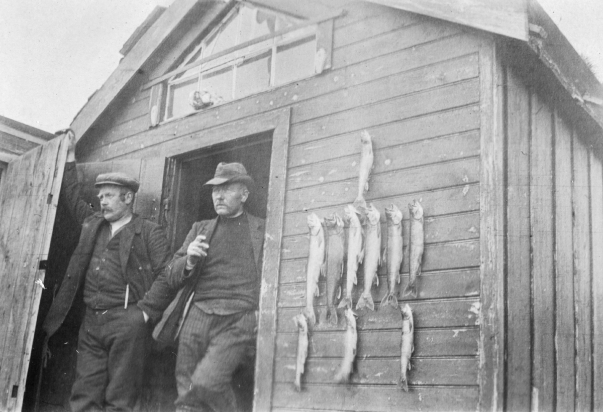 Blåsenborg 1915. To menn i døråpningen. Fisk henger på veggen.