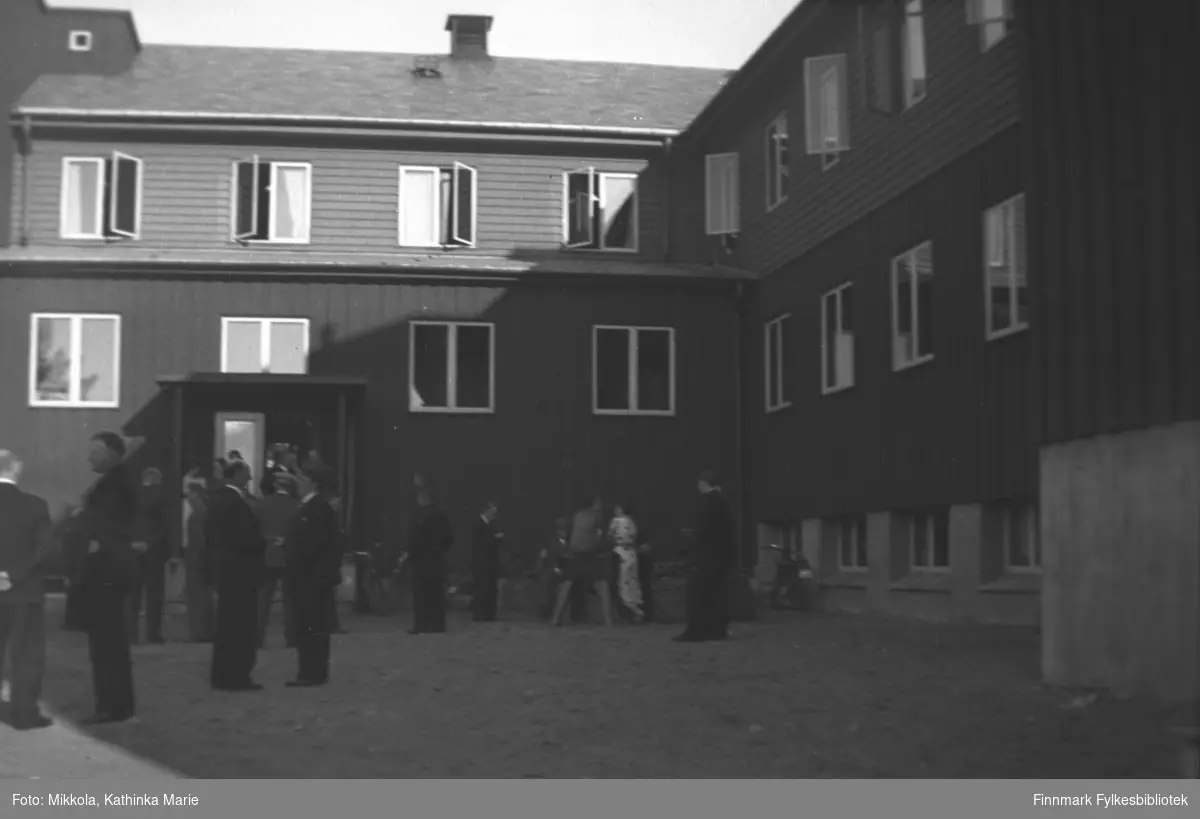 Sannsynligvis er dette Alta Gjestgiveri. Gjestgiveriene i Finnmark var på denne tiden drevet av Nord-Norsk Hotelldrift og kanskje også i Sørkjosen, men med unntak av Leif Johnsens Gjestgiveri i Rustefjelbma. På bildet ser man en rekke mennesker som står i grupper utenfor hotellet. 