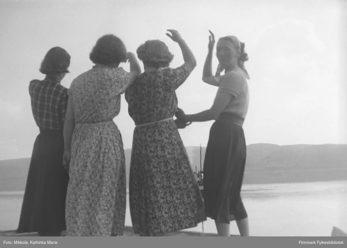 Fire sommerkledte kvinner med ryggen til fotografen på kaia på Mikkelsnes. De vinker til noen ute på sjøen. Marine Mikkola snur seg halvt mot fotografen