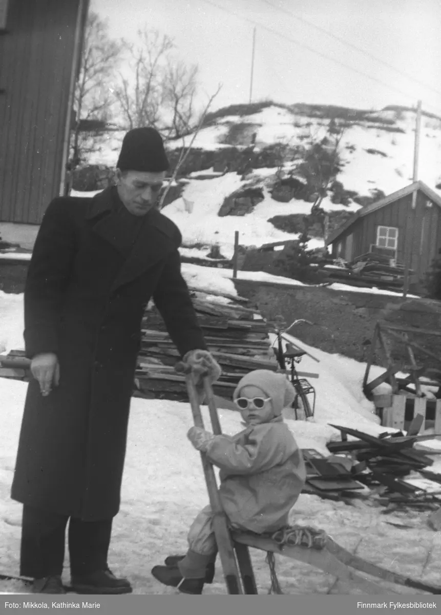 Sverre Olsen Lie med sønnen Sture på spark. Bildet er tatt på Haganes i gjenreisningstiden. Det ligger plankestabler og man ser spor av byggeaktivitet i bakgrunnen. Sverres mor Amanda bodde på Haganes