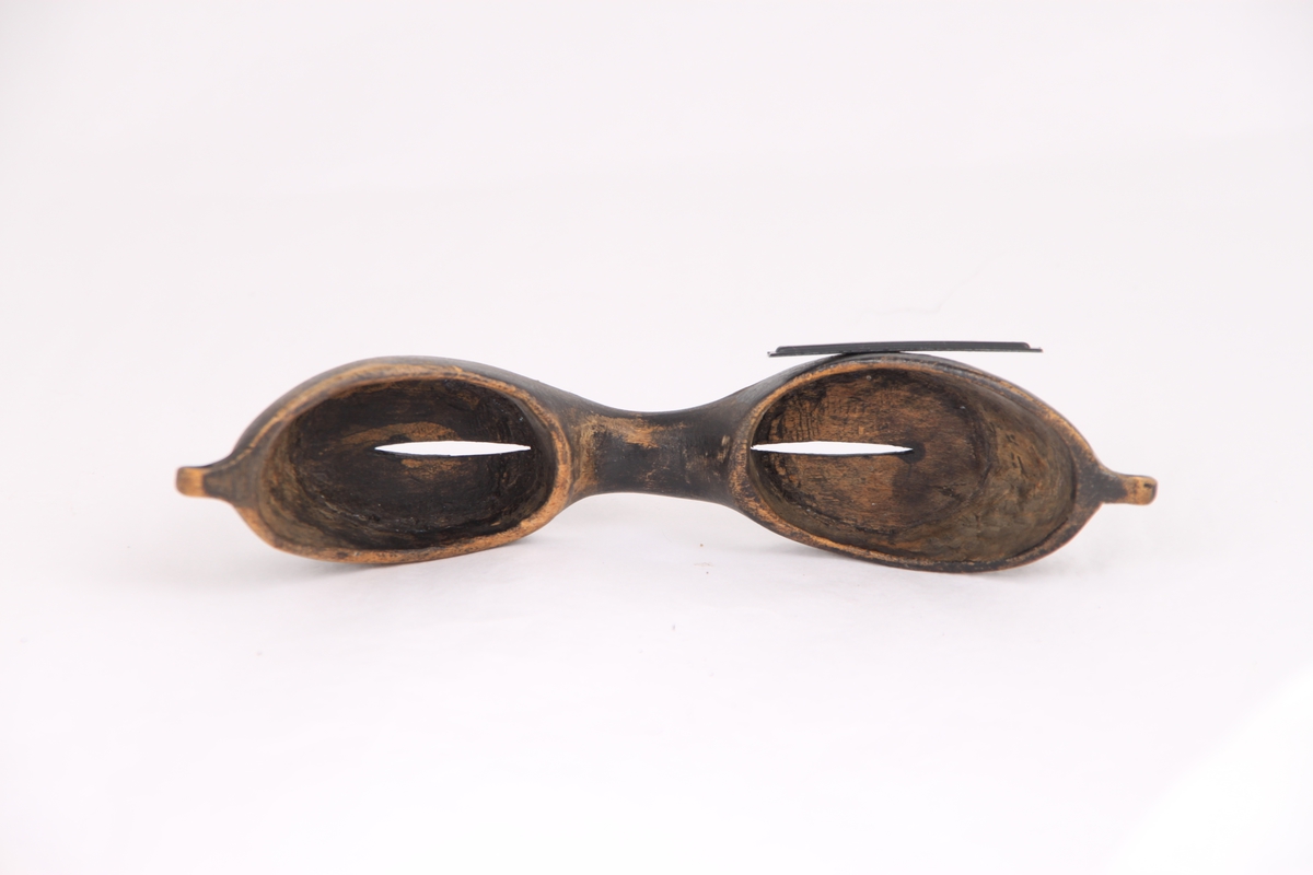 Snøbriller til beskyttelse mot snøblindhet i lett balsatre. Det er et hull til feste av snøre på hver side av brillen.