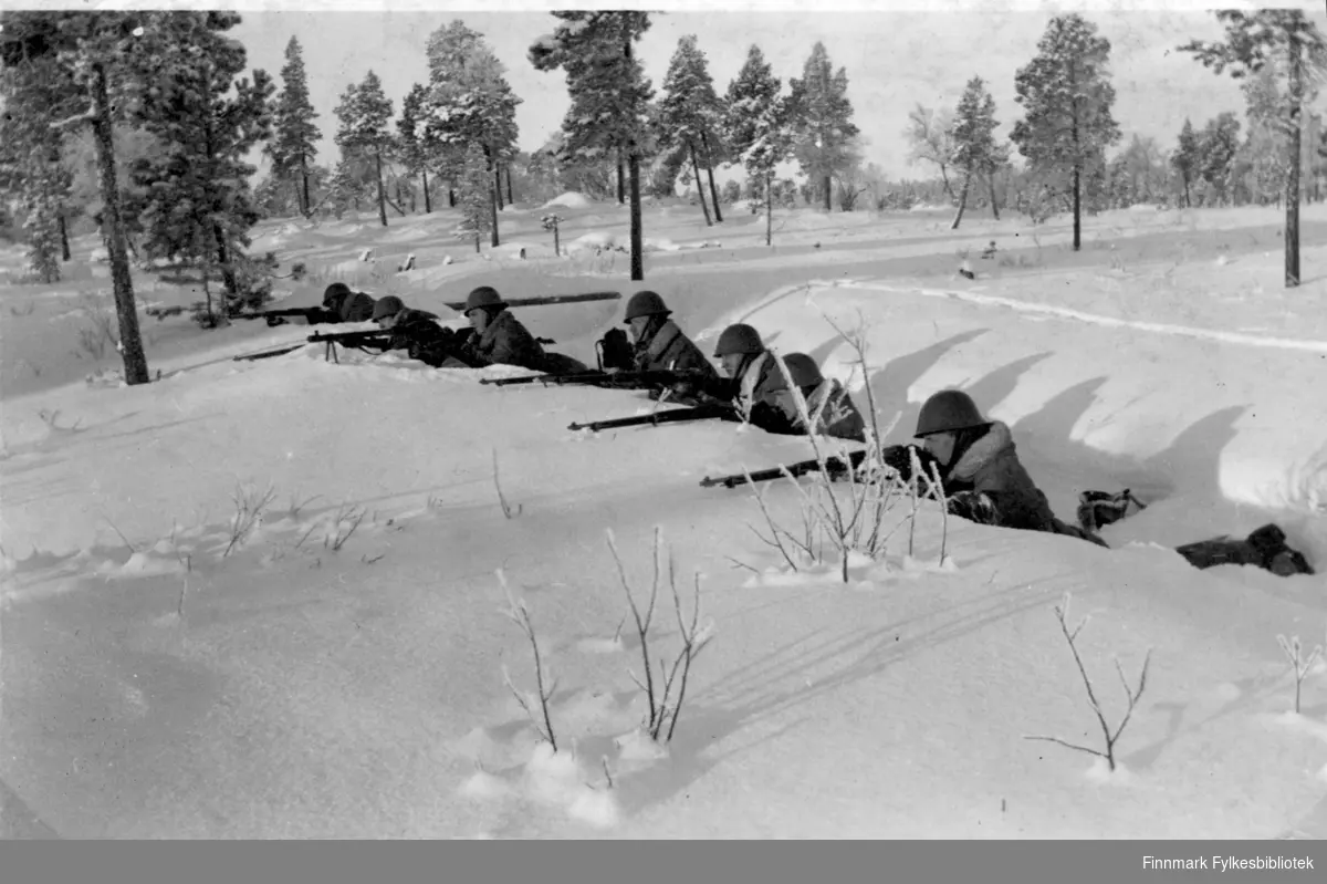 Soldater har øvelse i snøen, flere soldater ligger i skyttergraven og sikter med gevær.  Grensevakt, garnisonen i Sør-Varanger