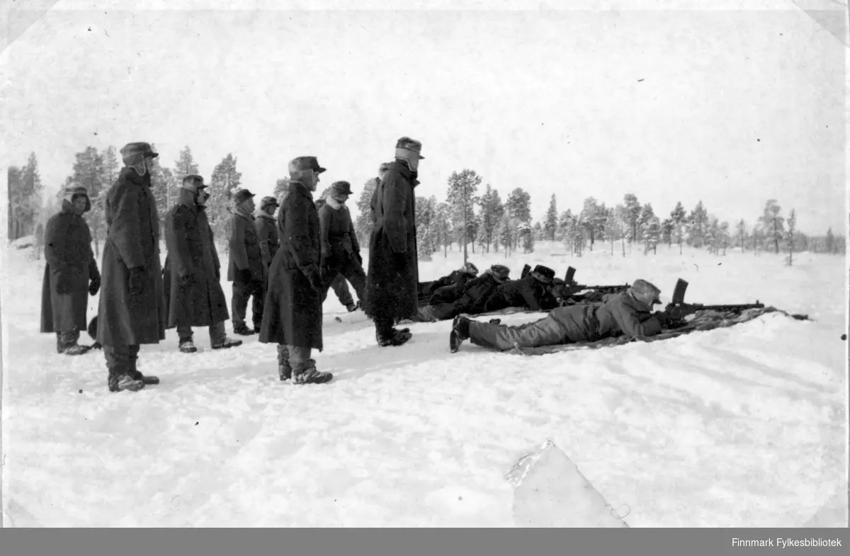 Soldater har øvelse i snøen, flere soldater står rundt, muligens av høyere rang.  Grensevakt, garnisonen i Sør-Varanger