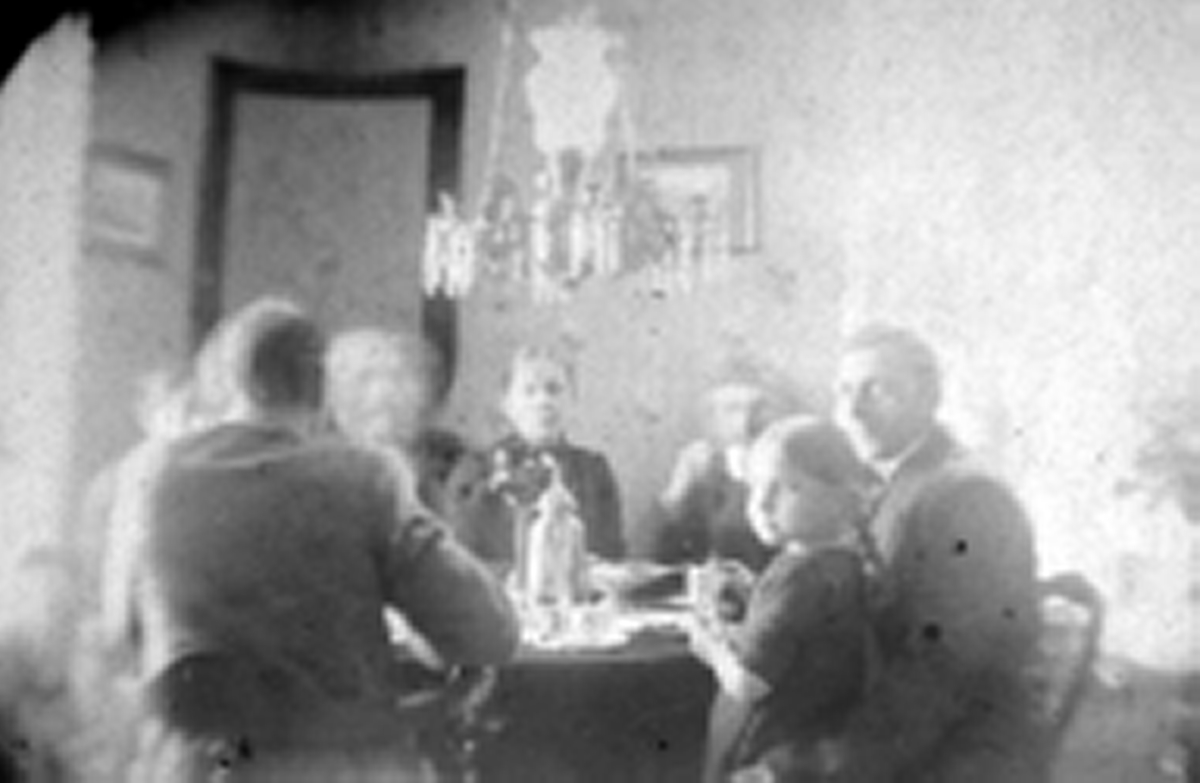 Håheim-familien i Neiden sitter rundt et bord. De fleste personene på bildet er ukjent, men mannen til høyre kan være Reidar Håheim. Han er kledd i jakke og slips. I hans fang sitter en en liten jente i kjole. Over bordet henger en lysekrone.