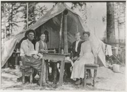 Fire personer rundt et bord utenfor et telt