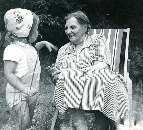 Sommaren 1955. Veronika i vit hätta med rosor. Judit Abrahamsson i klänning i franska flaggans färger. Sparkdräkten i ljusgult stickad av Birgit, babydockan ärvde den.