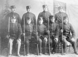 Portrettbilde av ni menn i uniform, soldater med gevær, atel