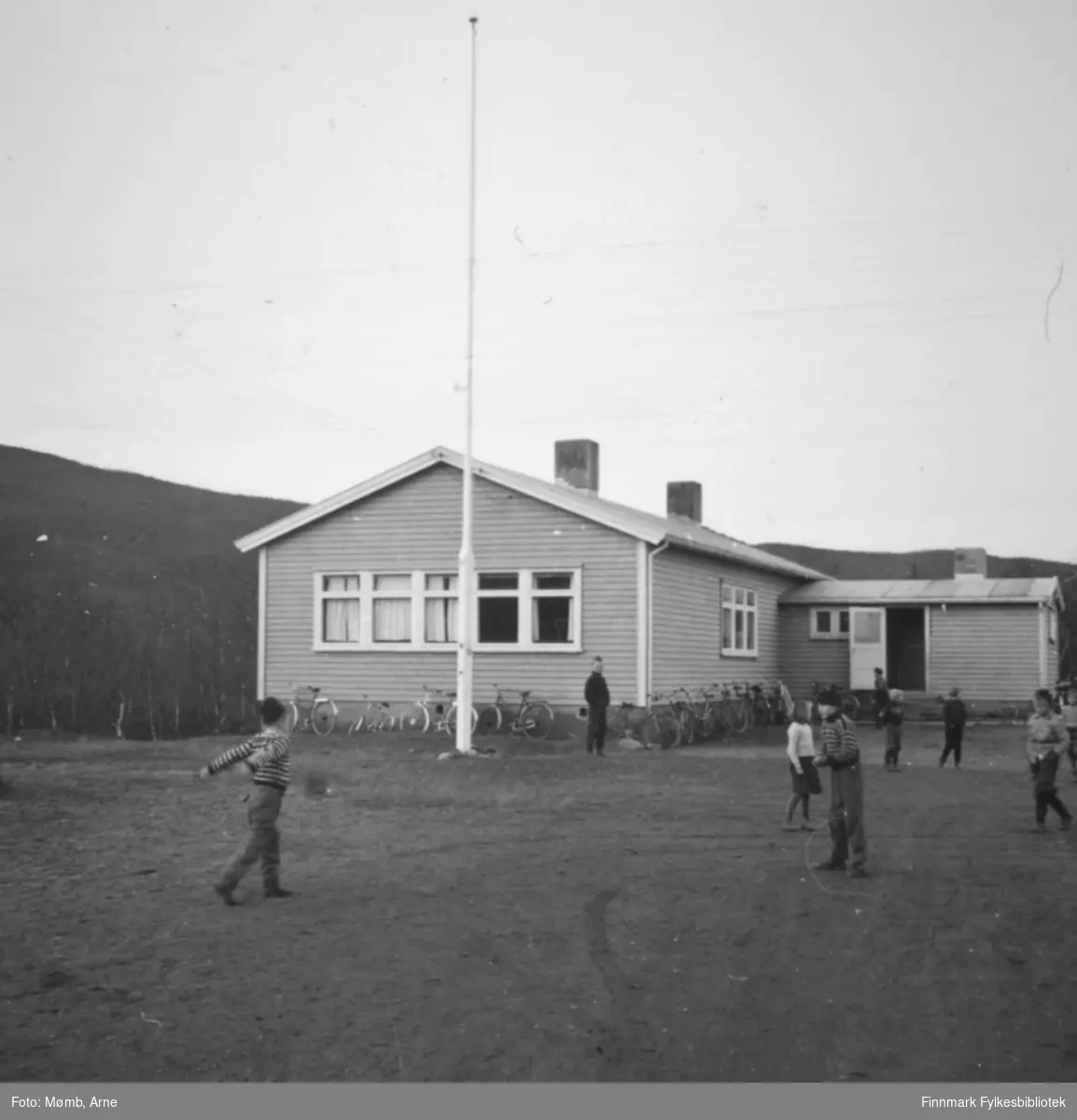 Boftsa skole, 1958. Barn leker i skolegården. Ved skolen kan man se flere sykler lent til veggen.