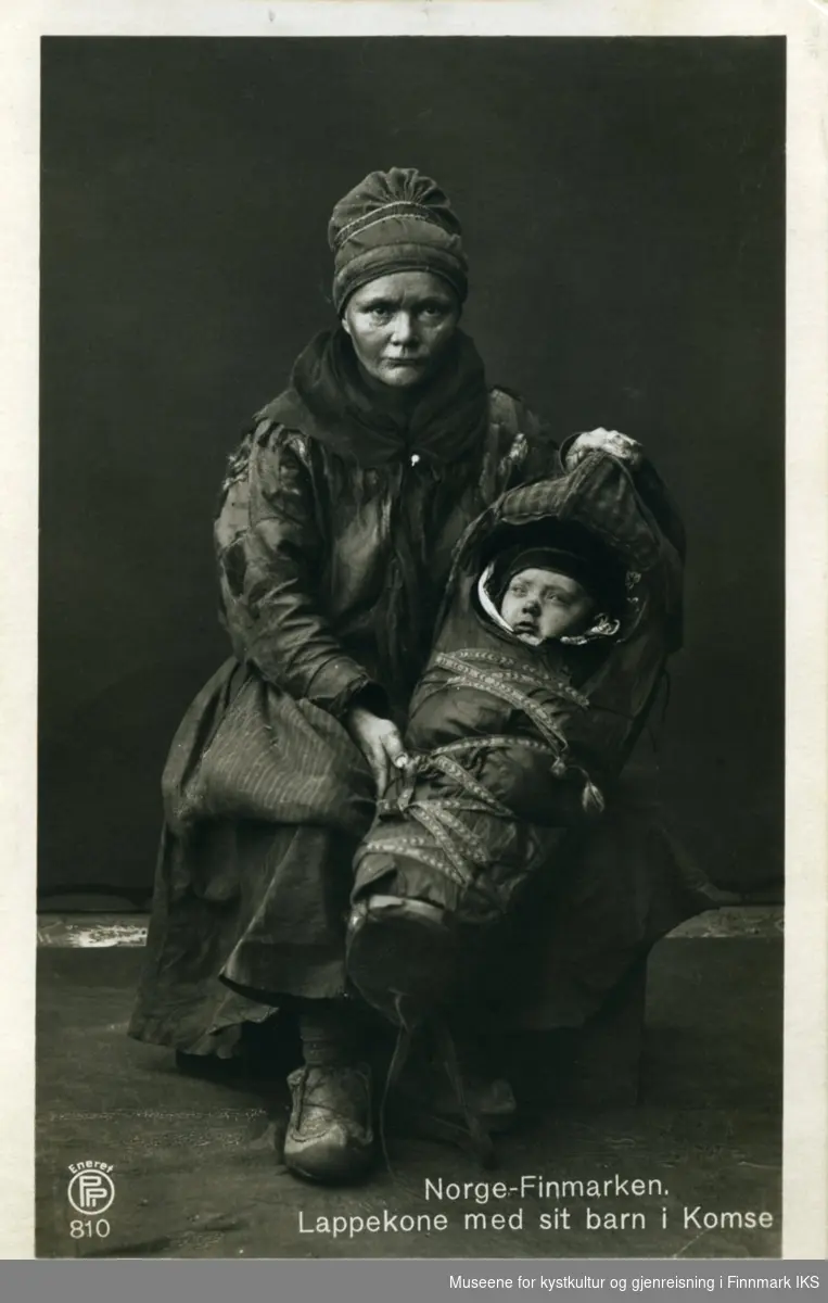 Postkort. Samisk kvinne med sitt barn i en komse.