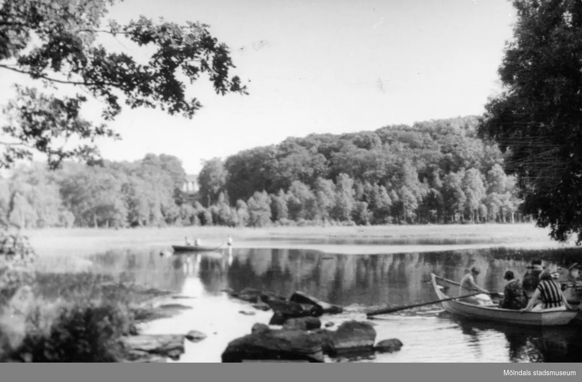 Vy över Stensjön, 1920-30-tal. Personer som ror ekor och en person som står i vattnet. I bakgrunden skymtas Gunnebo slott.