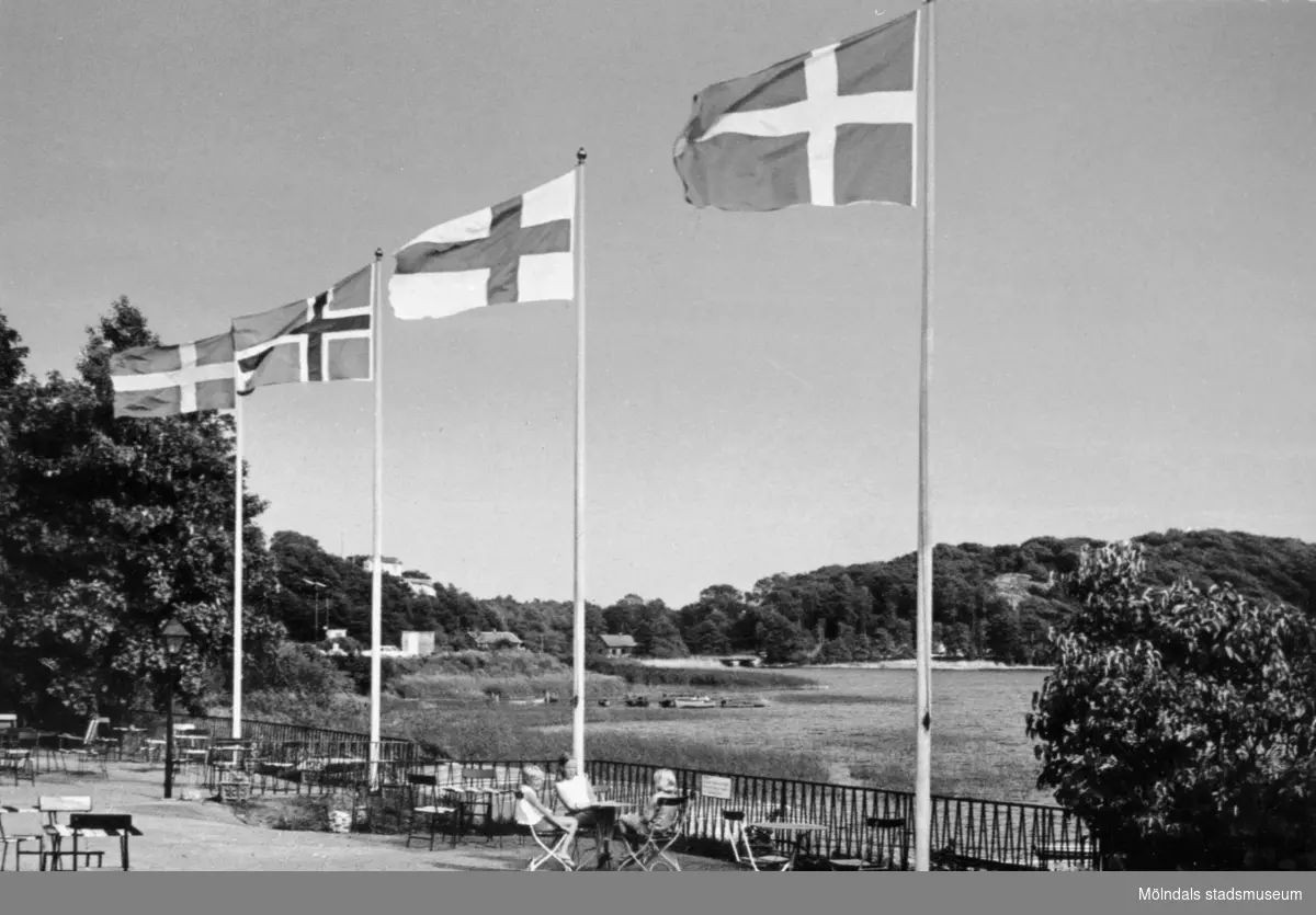 Vykort som visar de nordiska ländernas flaggor (förutom Islands) vid Stensjöns strandservering, 1970-tal. I bakgrunden Gunnebobro.