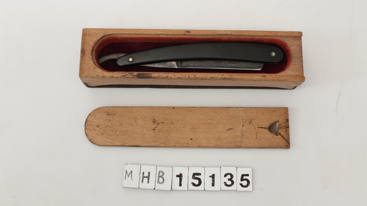 Barberkniv oppbevart i et treskrin med lokk. På baksiden av treskrinet er et slipeband til barberbladet.