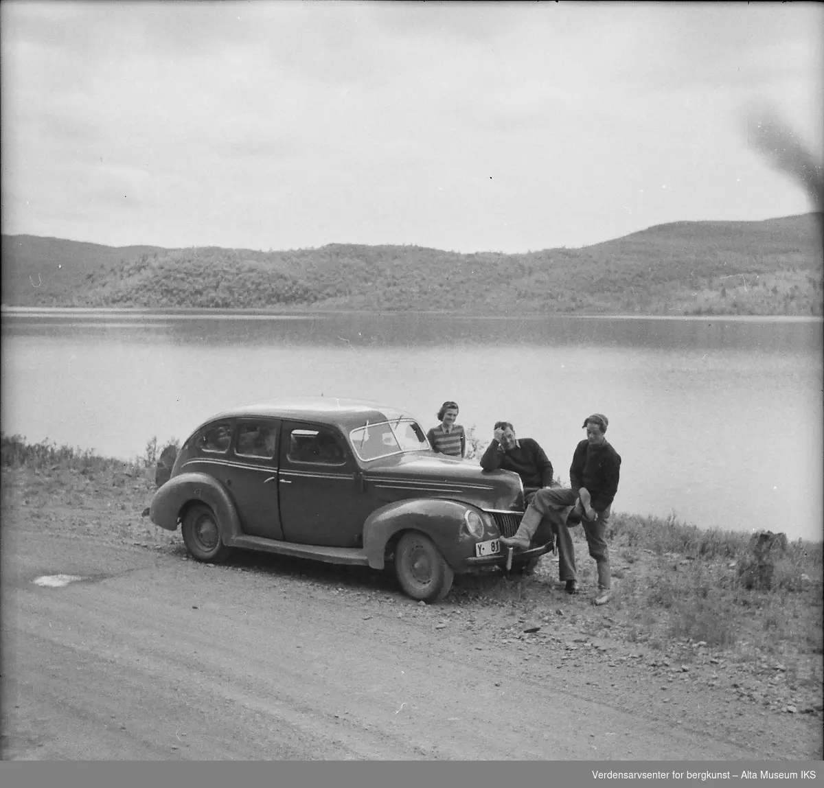 Tre unge reisende poserer med bilen foran en innsjø. Bildet er fra en Finlandstur.