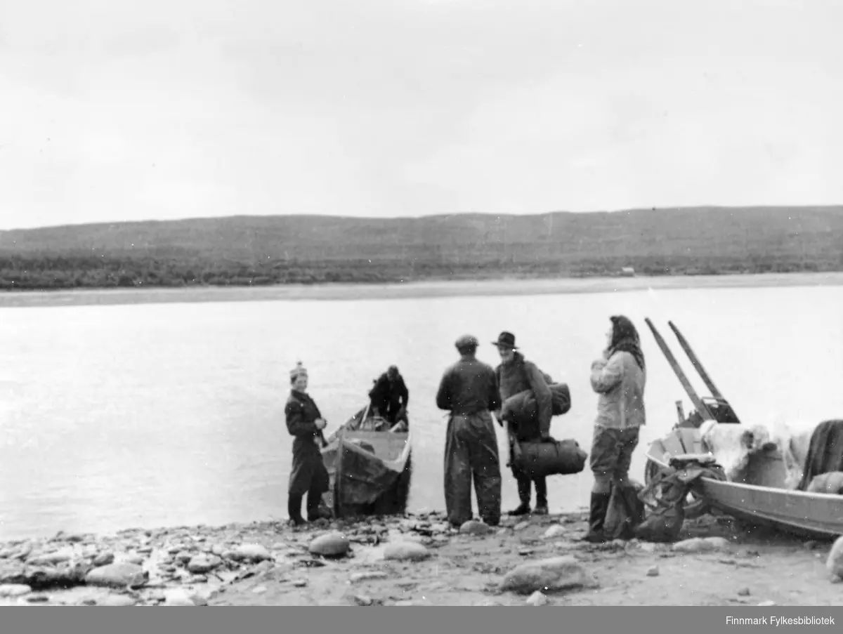 Skiippagurra, ved Tanaelva i 1947. Flere folk står i nærheten av elvebåter. Mannen som er nr. 2 f.h. holder på bagasje, og trolig er gruppen på tur mot Storfossen.