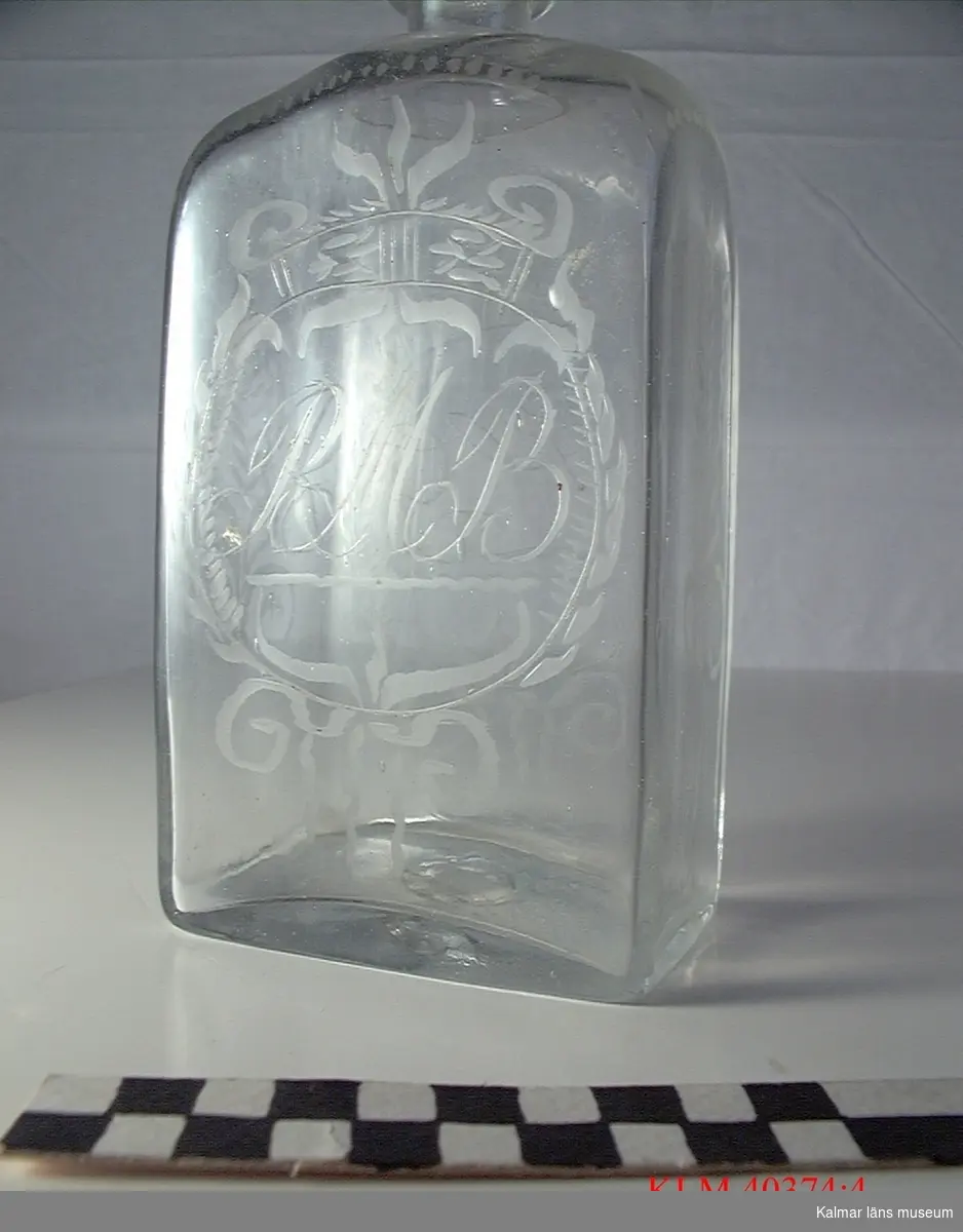 KLM 40374:4 Brännvinsflaska, ofärgat glas. Med graverad dekor: på ena sidan initialerna RMB, på andra ALG. Datering, 1700-tal.