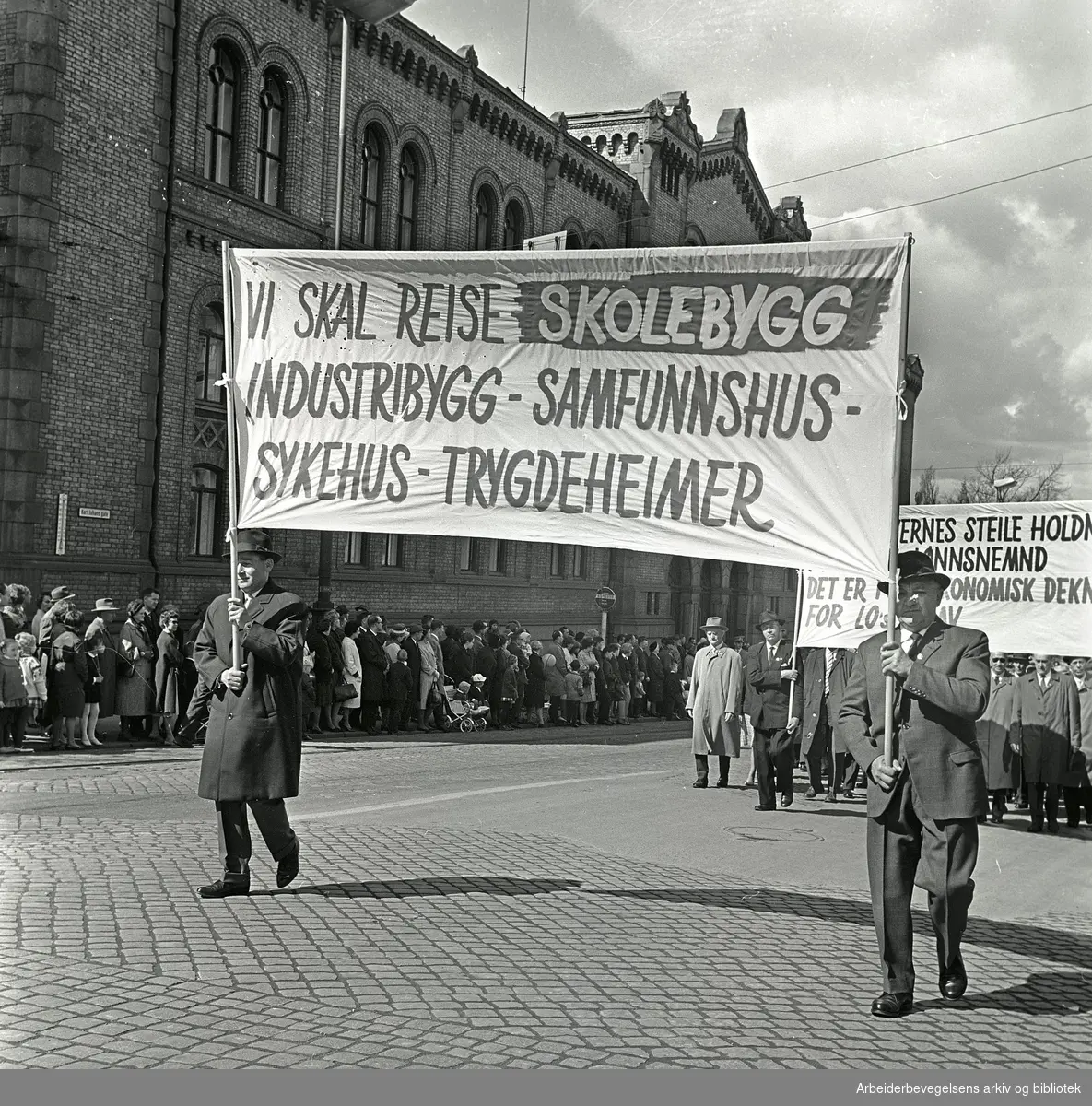 1. mai 1964 i Oslo.Demonstrasjonstoget i Karl Johans gate.Parole: Vi skal reise skolebygg - industribygg - samfunnshus - sykehus - trygdeheimer