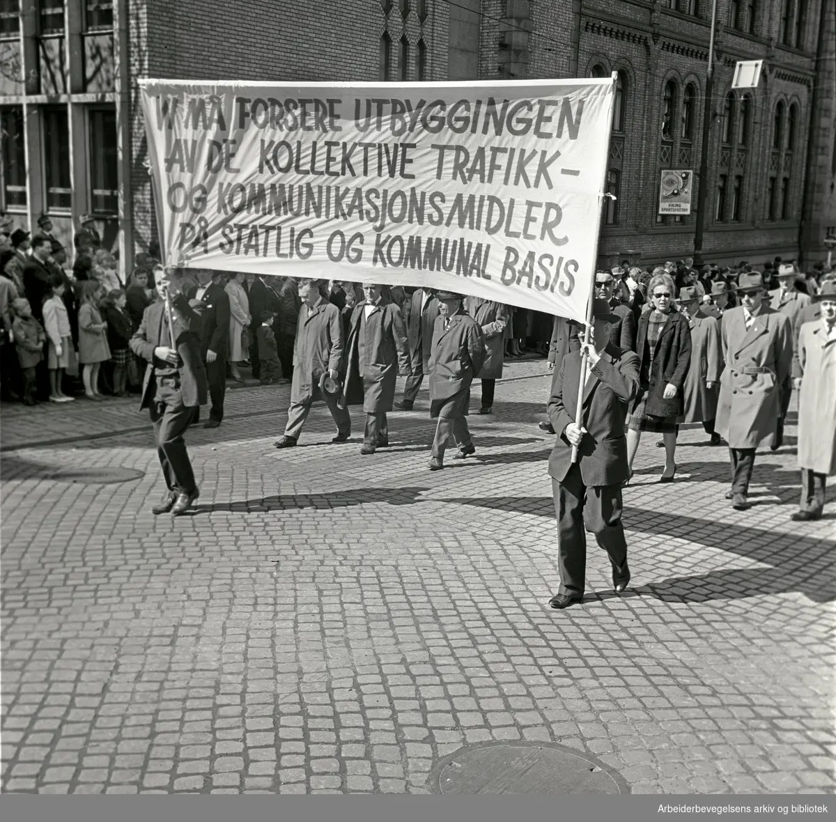 1. mai 1964 i Oslo.Demonstrasjonstoget i Karl Johans gate.Parole: Vi må forsere utbyggingen av de kollektive trafikk- og kommunikasjonsmidler på statlig og kommunal basis