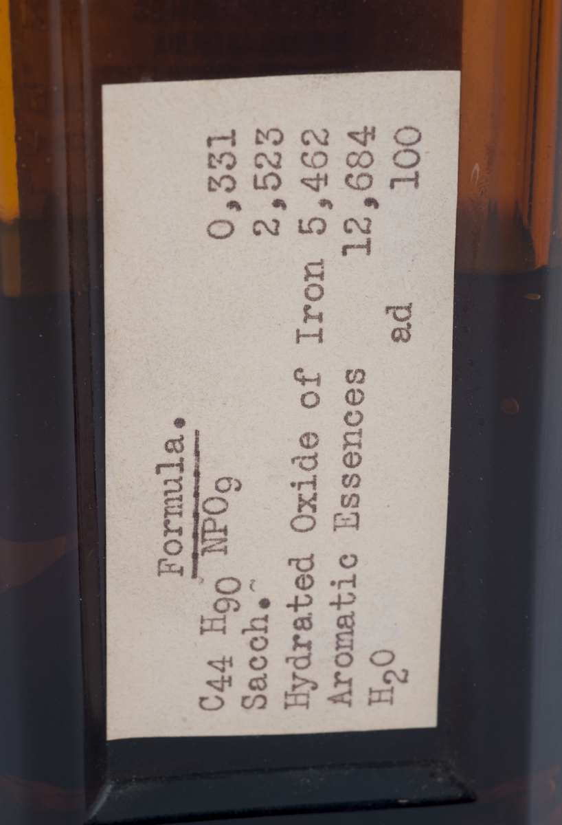 Rektangulær flaske med avrundete hjørner, og skrukork. Etikett over mesteparten av forsiden, adskilt med en mindre etikett med fabrukantens navn nederst. Etiketten er stemplet med: "12 aug. 1938". På baksiden maskinskrevet etikett med innholdstoffene.
Halvfull med mørk væske.