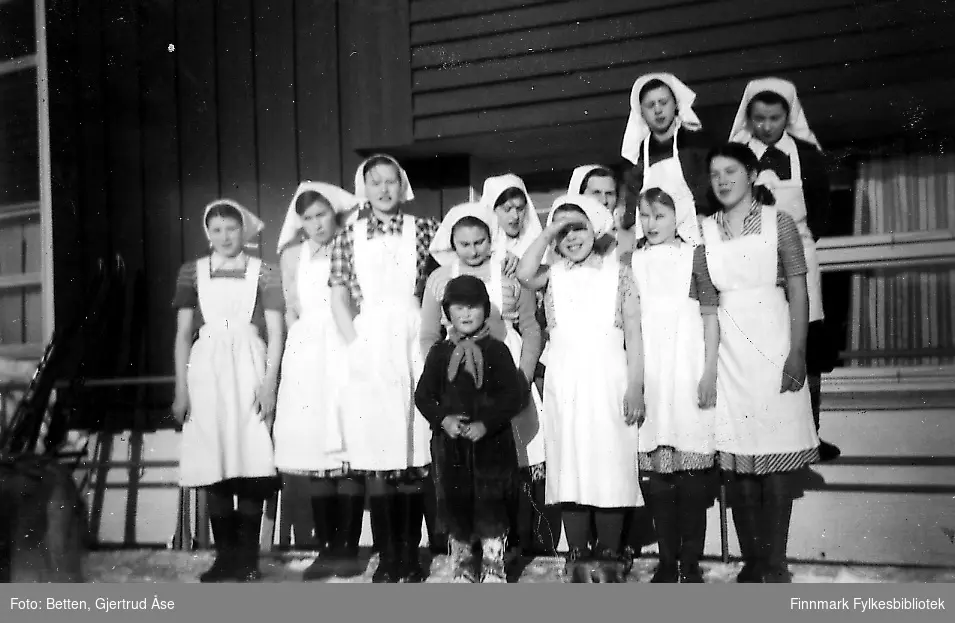 En klasse jenter står på trappa på skolen i Seida. Jentene har på seg hvite forklær og hvite tørkler. Dem er fra Boftsa skole og i husholdopplæring i Seida. En liten gutt står foran dem.