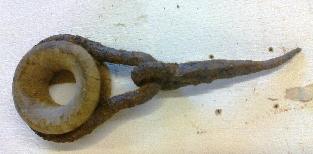 Rund treblokk/ring satt inn i ei pæreforma jernbeslått bøyle med festespiker forma som ein pigg med auge i eine enden.