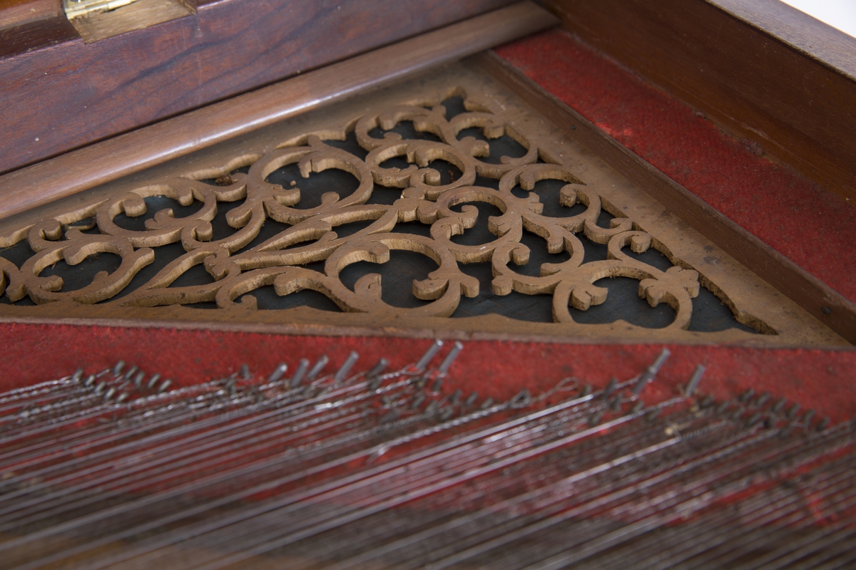 Taffelpiano med seks dreide ben med hjul. Skåret ornamentikk ved tangenter og på innsiden. Sammenbretbart notestativ.