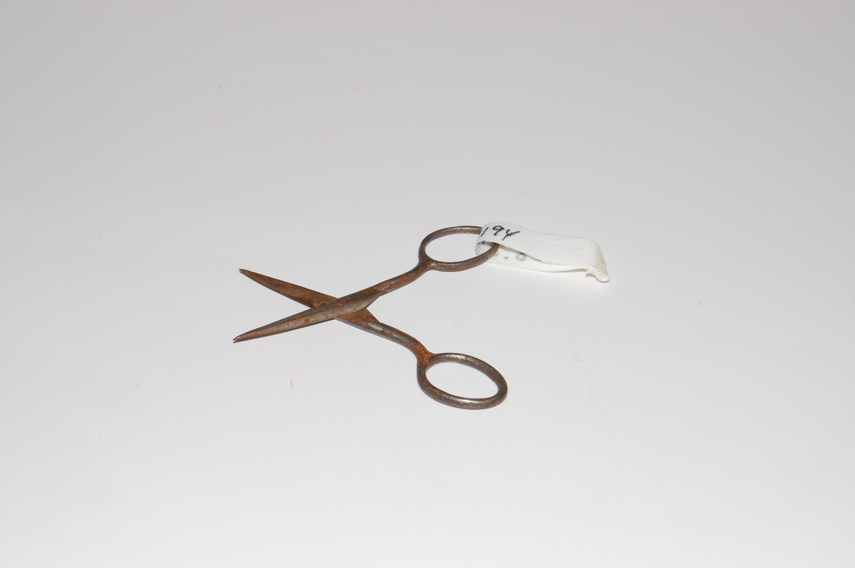 Form: To like deler som krysser hverandre: Saksblad med håndtak formet som sløyfe i enden. 
