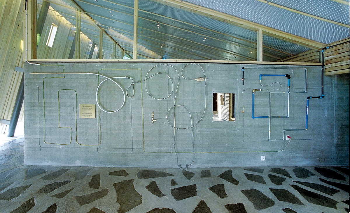 Elementene i installasjonen utgjør et tegnet mønster som assosierer både til et industrielt scenario og til labyrinten, uten at det umiddelbart lar seg entydig gripe. Flere steder er rør malt blå, gule og grønne, som reflekterer lyset som sprer seg øverst i rommet gjennom de tilsvarende fargede vindusglassene. Dette bidrar til å skape en estetisk og poetisk dialog mellom kunsten og bygget. På betongveggen finner man spredte hverdagsgjenstander slik som et speil, et forseggjort messingdørhåndtak, en stikkontakt, samt elementer fra naturen i form av et vakkert sammenfoldet skjell, bambus og trestykker. Fra fondveggen strekker installasjonen seg videre i ulike retninger bortover langs de tilstøtende veggene og avsluttes på forskjellig vis, som for eksempel i kunstnerens personlige pilspiss, godt bevart fra egen barndom. En av linjene bryter tvers gjennom bygningsveggen og fortsetter videre i utomhusterrenget i det utvendige inngangspartiet. Der løper den langs bakken, kryper oppover en stor granittstein som kunstneren har hentet fra den lokale elvebredden og videre langs bakken, for til sist å forsvinne ned i jorden.

En messingplate til venstre på fondveggen har det indianske ordtaket «Det er syv hovedretninger: Opp, Øst, Sør, Nord, Vest, Ned og Inn i Deg Selv» innrisset på samisk og norsk som gir oss et utgangspunkt for egne tolkninger. Linjene i installasjonen har noe med retningene å gjøre for de ulike gjenstandene er metaforer. I speilet møter du deg selv, og med håndtaket kan du åpne dører og grenser. Pilen peker mot skogene som symboliserer en del av menneskenes naturlige røtter, vår fruktbarhet er knyttet til jorden og steinen er det eviges symbol.