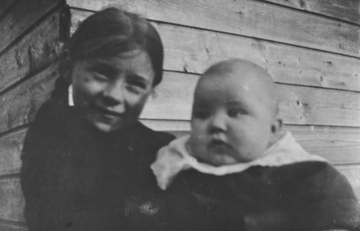 Bilde av Lilly Lein med lillebror Rolf. Hun i mørke klær og fletter, Han med stor hvit krave.Vi ser litt av en bygning bak.