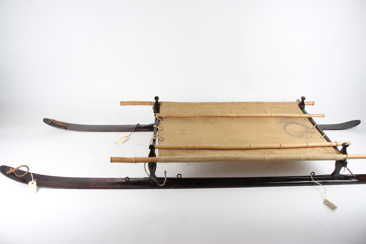 Skikjelke for en person med meier i tjærebeiset tre. Pulkens "sete" er av seilduk, spent over en ramme av blant annet bambusstenger.
