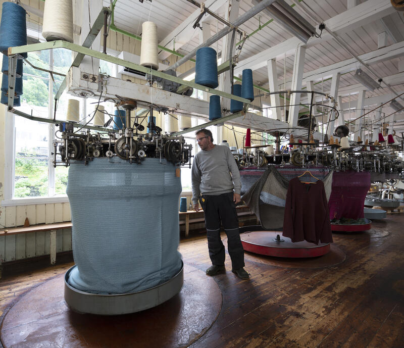 store strikkemaskiner i gammalt fabrikklokale, mann arbeider med maskin