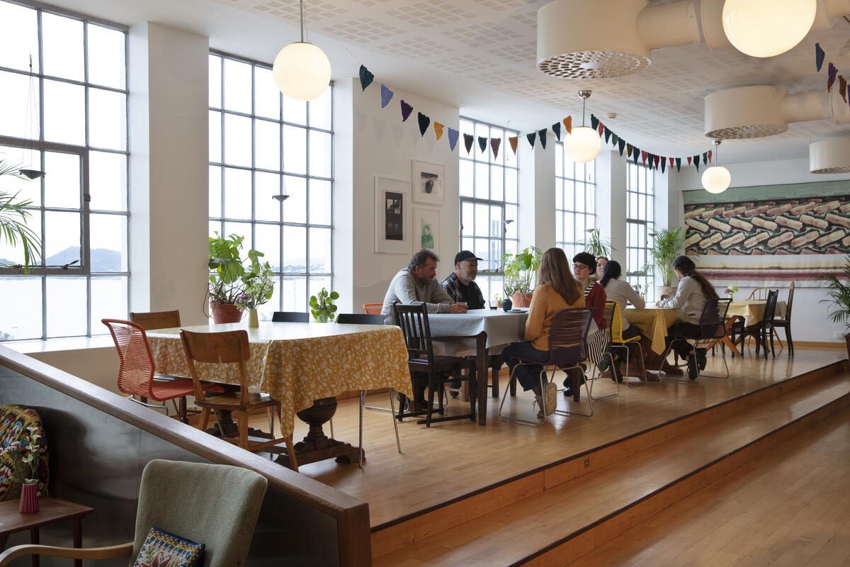 kafélokale med gjestar, stolar og bord, store fabrikkvindauge (Foto/Photo)