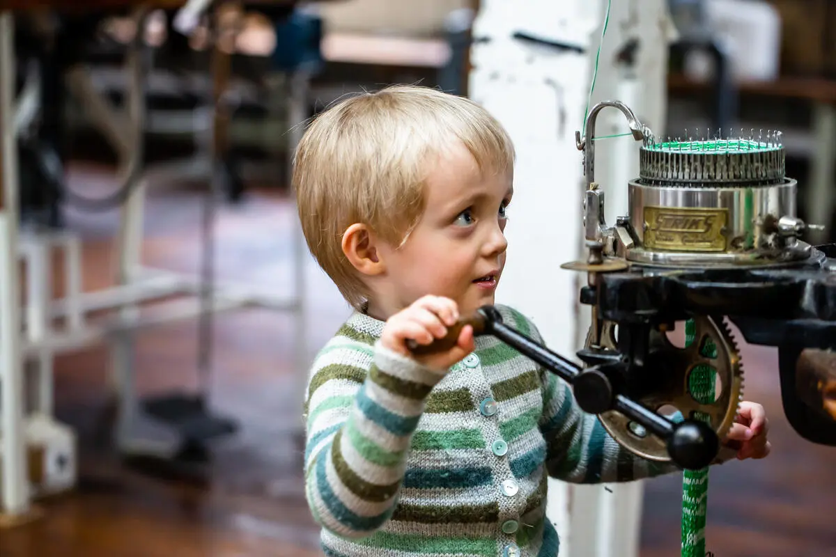 boy in knitted sweater operates knitting machine at The Textile Industry Museum