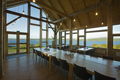 Interiør med langbord, vindauge med utsikt over kystlandskap. Foto. Foto/Photo